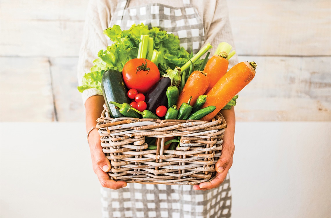 person carrying woven basket full of vegetables.