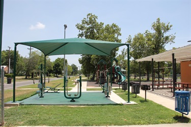 Fitness stations in the foreground can be used as an outdoor gym. There is a playground with slides in the background.