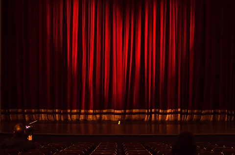 Empty theater seats and stage with a closed red curtain.