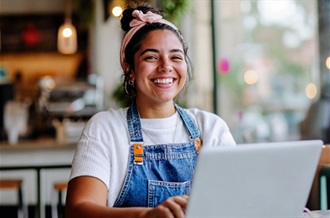 A woman with a cheerful expression uses her laptop, reflecting a positive and productive moment.