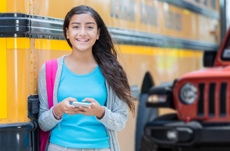 young person on cell cell phone standing in front of a yellow school bus and orange jeep