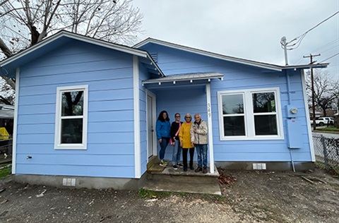 Four people standing the doorway of a blue house.