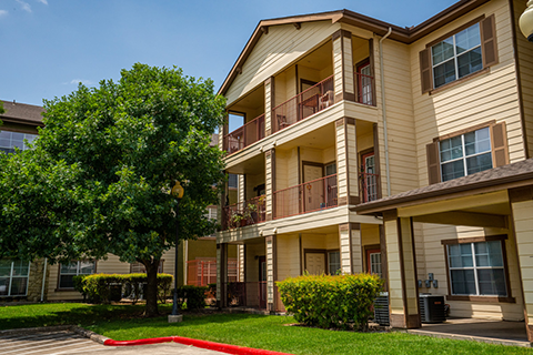 Midcrown Senior Pavilion is a three-story apartment complex with predominantly light beige siding, darker brown trim on windows and includes balconies, landscaping and mature trees.