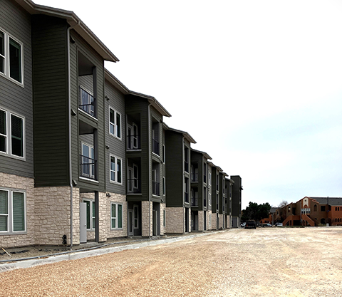 Sunstone Apartments is a multi-level complex with dark grey siding and white brick accents. The complex also includes balconies.