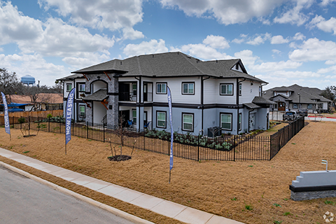 Vista at Silver Oaks is a multi-level apartment complex with white siding, light blue accents and grey brick columns. The complex has newly, planted trees and landscaping throughout.