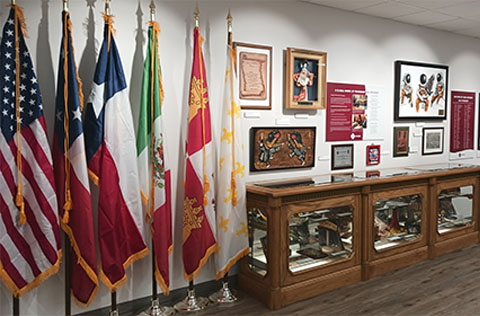 An exhibit featuring 6 flags. There are framed historical documents and photographs, and a case filled with artifacts.