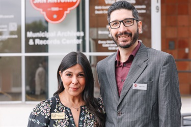 A museum curator and archivist standing together in front of the museum entrance, smiling at the camera.