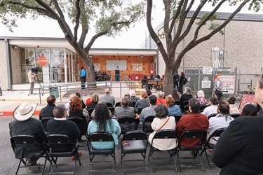 Audience seated outdoors in front of the Municipal Archives Museum as the City Clerk speaks at a podium during the Grand Opening.