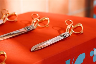 Close-up of two ceremonial ribbon cutting scissors placed on a table, with a City of San Antonio tablecloth partially visible.