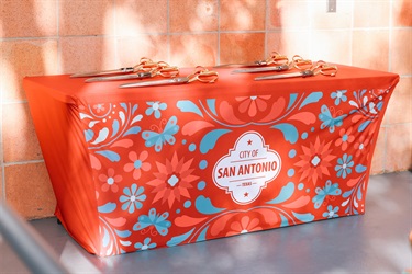 A table covered with a City of San Antonio tablecloth, displaying six ceremonial scissors arranged for a ribbon cutting event.