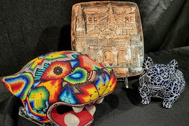 A colorful, beaded jaguar and a blue ceramic jaguar flank a plaque with a Church engraved. Each is from Mexico.
