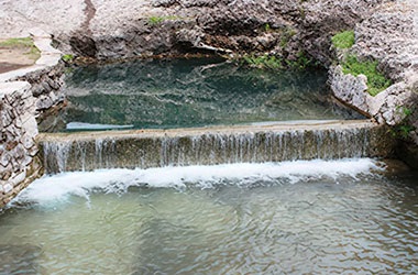 A waterfall cascades into a river at San Pedro Springs.