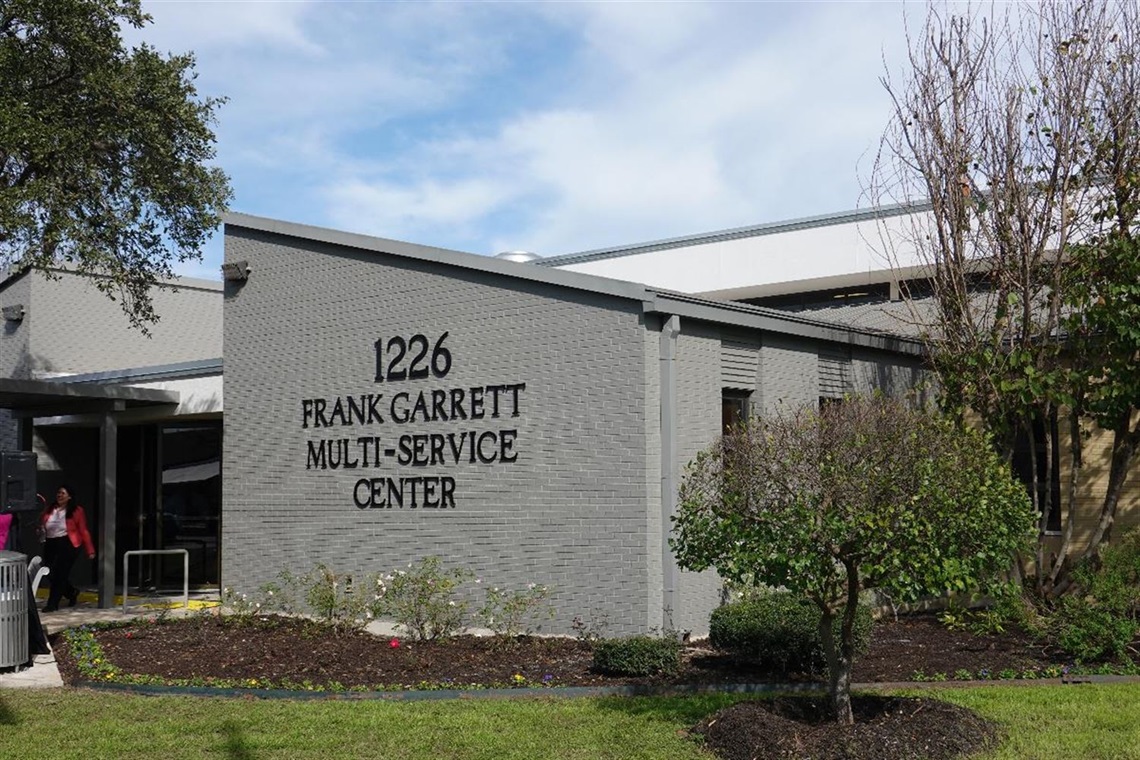 A grey building surrounded by trees and bushes.