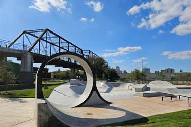 A skate park featuring a curved ramp and a bridge in the background.