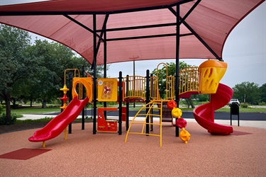 A large playground with red slides and climbing bars under red shade canopy
