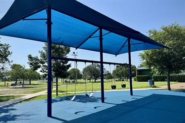 Blue swing set under a canopy, surrounded by trees and open grassy areas.