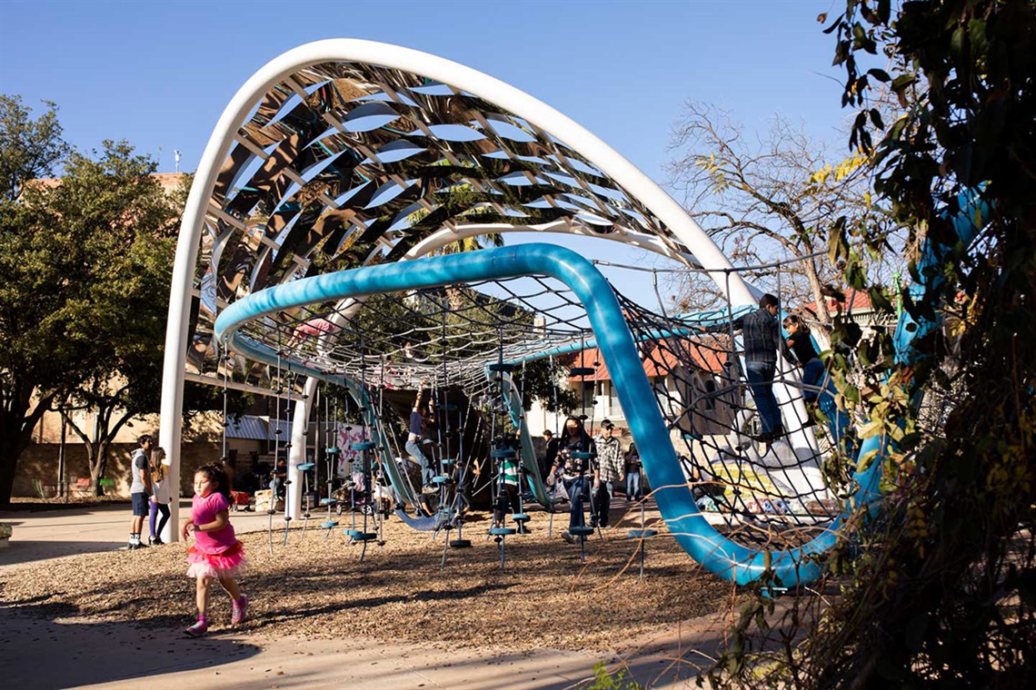 A child joyfully plays on a blue playground structure, climbing and exploring the various features.