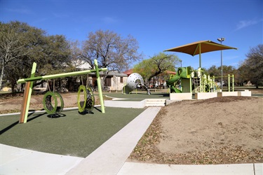 A playground with a slide and swings, covered by a protective canopy for shade.