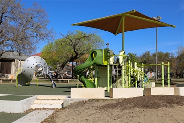A playground with a slide, covered by a protective canopy for shade.