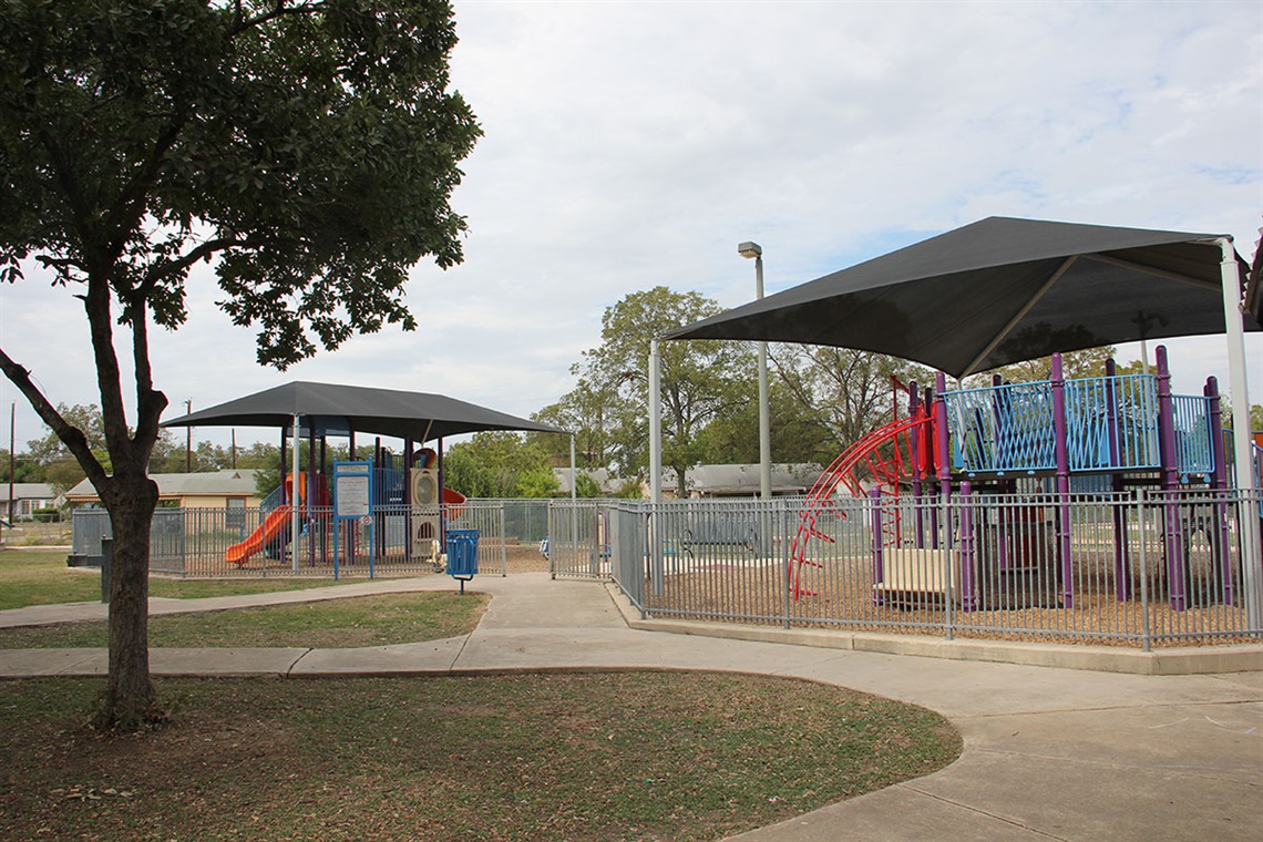 Two playgrounds, paved walkway, tree and recycle bin