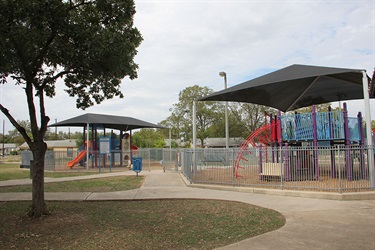 Two playgrounds, paved walkway, tree and recycle bin