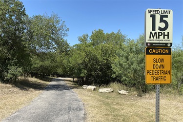 Road in between trees with speed limit and caution sign