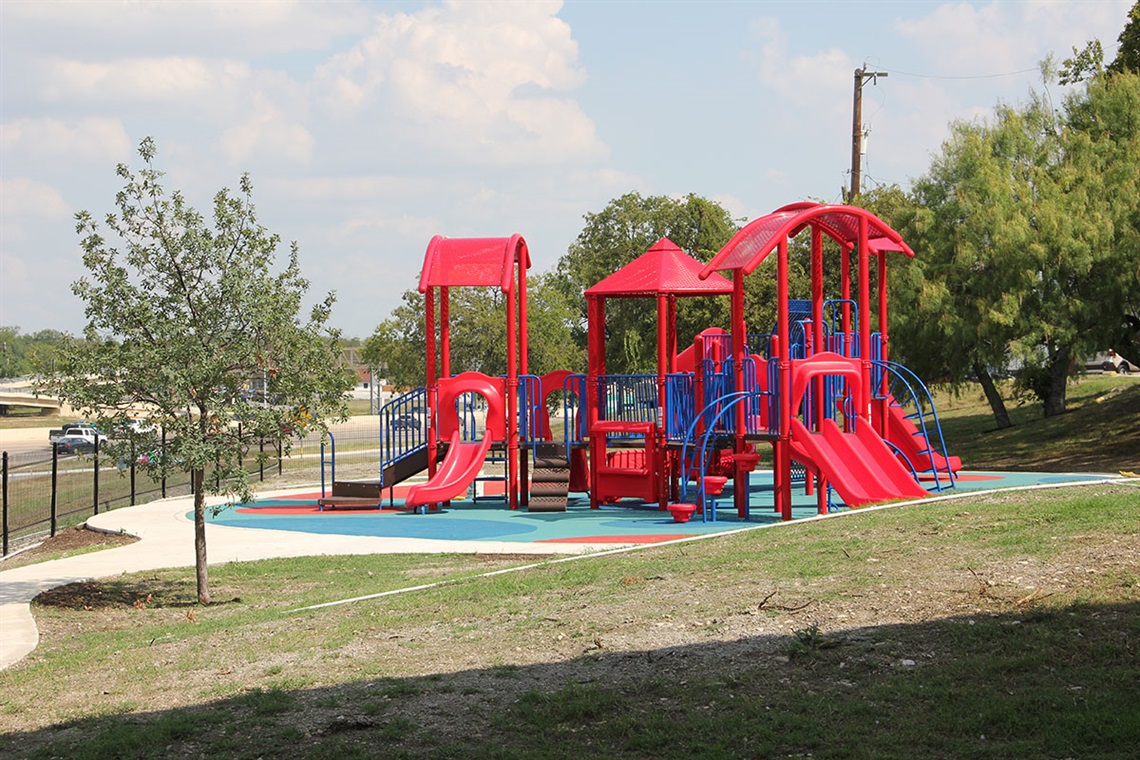 Red and blue playground equipment with a paved walkway