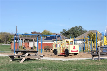 An outdoor playground featuring swings, a bus, and a picnic table.
