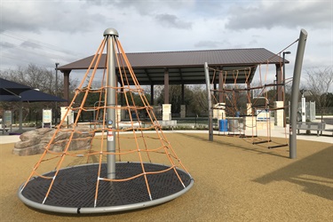 Playground with rope bridge and climbing structure on merry-go-round.