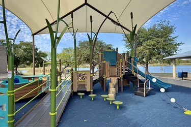 A nautical themed playground with boat-like features and slides, shaded by a canopy.