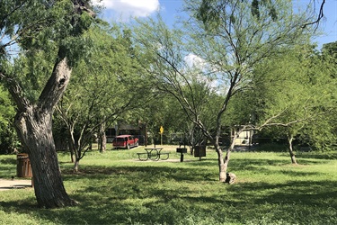 A serene park with lush trees, green grass, and a red car visible in the distance.