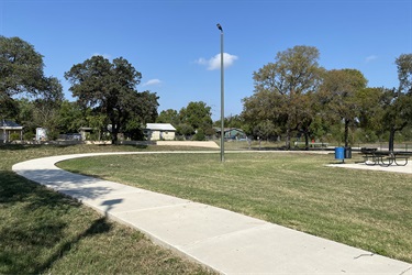 A serene park with a paved sidewalk and inviting benches in the middle of a lush green grass area.