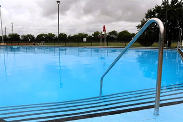 A bright blue swimming pool with a metal handrail and steps leading into the water. 