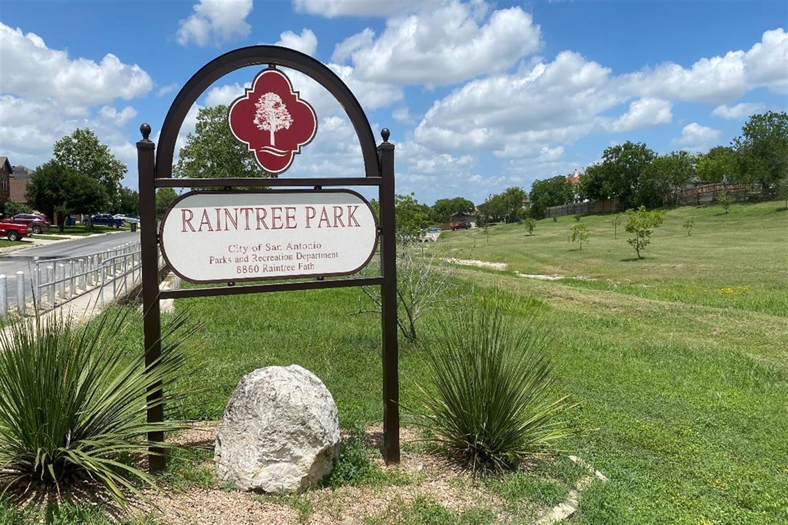 Raintree Park sign with grass in background.