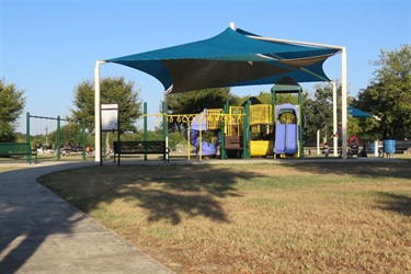 A playground with a blue canopy providing shade.