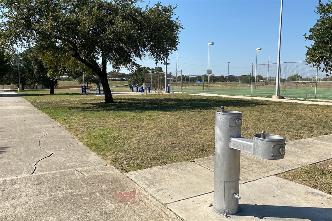Water fountain in park with Blue Fitness Station in background.
