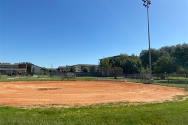 A baseball field with a light pole in the center, surrounded by dirt.