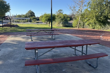 Two red picnic tables on concrete.