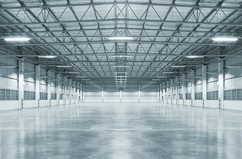 An empty warehouse featuring bare concrete floors and a high ceiling, creating a spacious and industrial atmosphere.