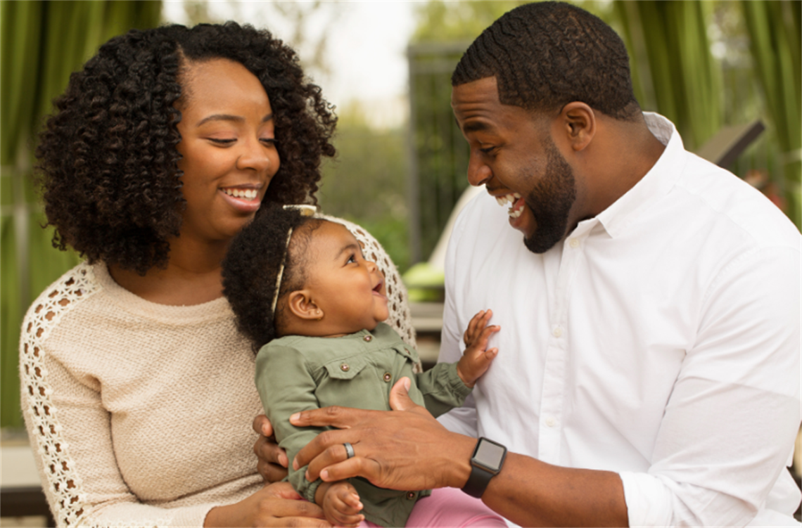 A young couple smiling with their baby.
