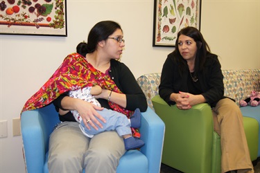 Mother breastfeeding covered baby and talking with Lactation Support employee
