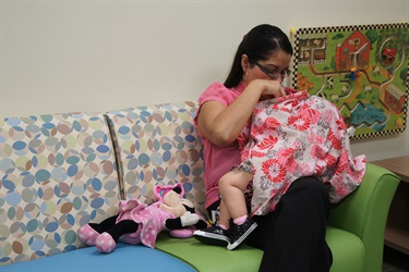 Mother breastfeeding covered baby on green couch with Minnie Mouse doll next to her right