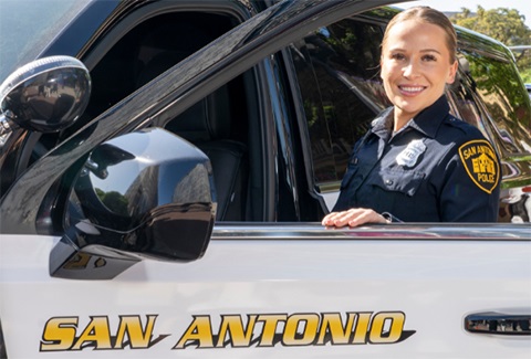 Female SAPD officer standing next to a SAPD police car.