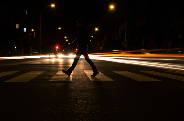 A person crossing a dimly lit crosswalk on a street at night, illuminated by streetlights.