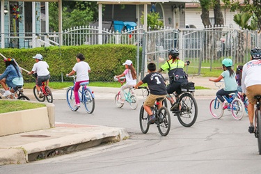 A police officer cycles with a group of children riding bikes through a neighborhood street.
