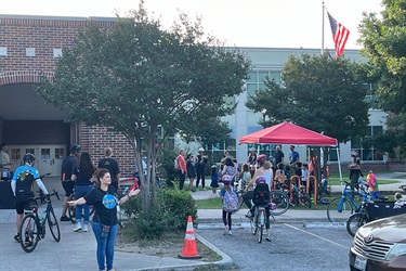 Families and cyclists gather outside a school with bikes and a tent set up during a community event.