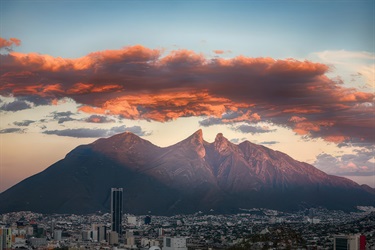 Cloudy, sunset image of Cerro de la Silla Mountain Range and below city of Monterrey, Mexico.