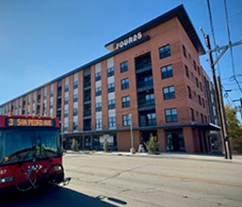 Corner building featuring brick walls, big windows, and greenery by the entrance.