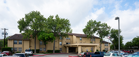 Pecan Hill Apartments are up to three stories, are a light beige stucco and include accessible parking, some landscaping and mature trees.