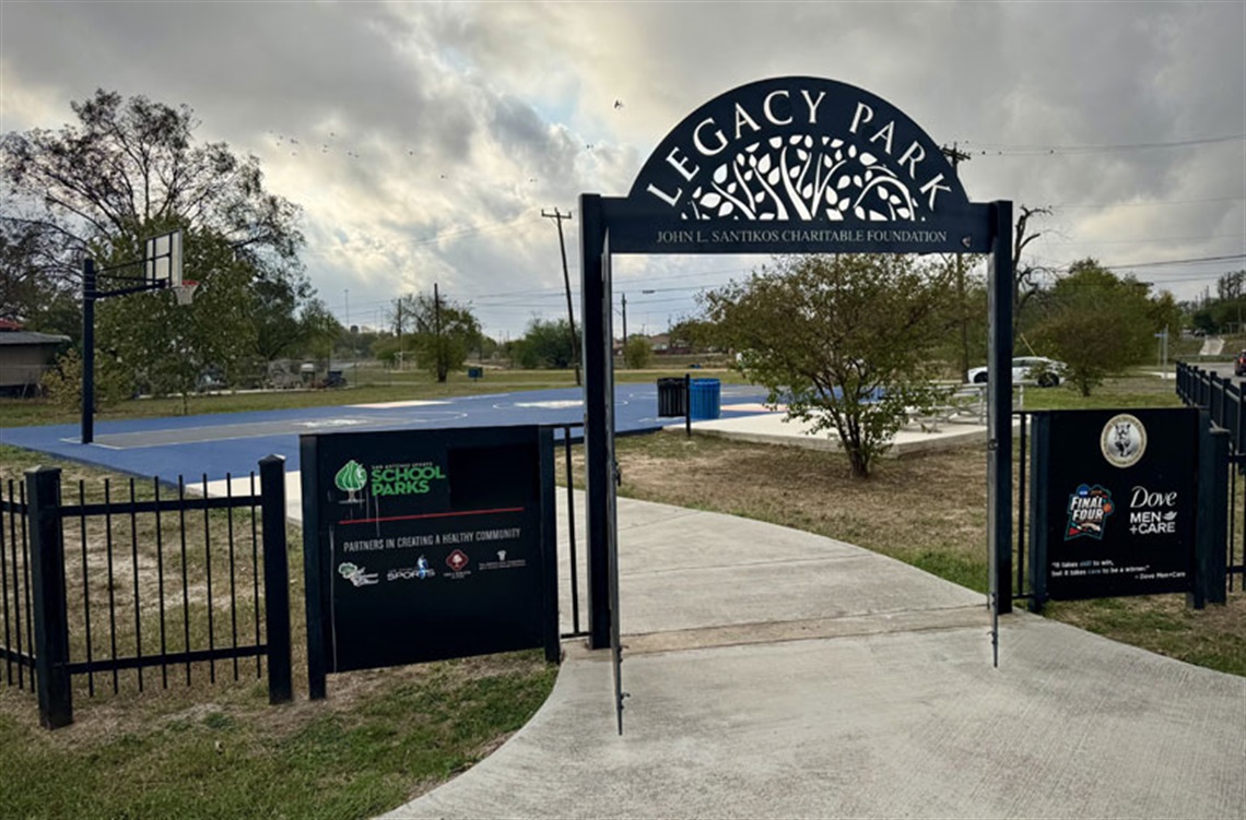 An entrance with a sign on top that says Legacy Park, that leads to a basketball court visible in the background..